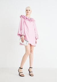 Ροζ κοντό φόρεμα με ρυάκι στο λαιμό και πτυχωτά, καμπυλωτά μανίκια; σε συνδυασμό με μια ασημένια τσάντα φάκελο και μαύρες πλατφόρμες με λουριά.