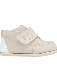 Zapato de lona beige con una correa de velcro, punta redondeada, parte superior texturizada y suela de goma blanca. Presenta un detalle de logotipo circular.