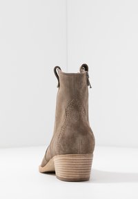 Stivaletto in suede marrone con tacco basso a blocco, dotato di zip laterali, linguette per l'estrazione e dettagli di cucitura a contrasto.