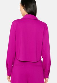 Fuchsia cropped blouse with a collar and long sleeves, featuring buttoned cuffs and a smooth texture. Minimalist design with no patterns.