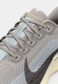 Primer plano de zapato de correr Nike en gris claro y azul con parte superior de punto texturizado y logo de swoosh negro en el lateral.