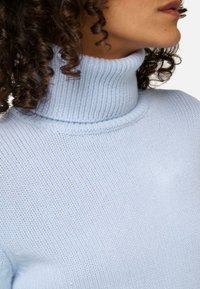Pull en tricot col roulé bleu clair avec un col côtelé et une texture douce, au design ajusté qui souligne le cou et les épaules.