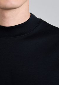 Svart sweatshirt med hög, ribbad halsringning och jämn textur. Tyget verkar mjukt, med minimala synliga sömmar och inga mönster.