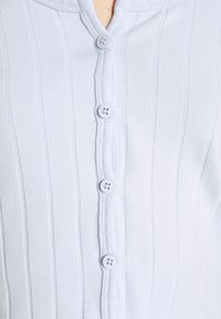 Světle modrý žebrovaný cardigán s légou se šesti jemnými bílými knoflíky a měkkou strukturou. Zakulacený límec, přiléhavý střih.