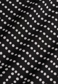 Tissu noir avec des pois blancs espacés régulièrement disposés en rangées diagonales, montrant de légères rides et une texture.