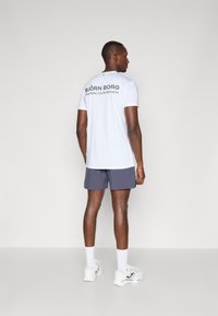 Valge lühikeste varrukatega T-särk, mille seljal on kiri "BJÖRN BORG TRAINING CLUB MONACO", kombineeritud hallide lühikesed püksid ja valged tossud.