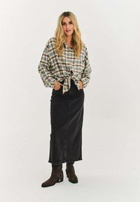 Kostkovaná košile na knoflíky v béžové a zelené barvě, zavázaná v pase, kombinovaná s černou džínovou maxi sukní a hnědými kozačkami po kolena.