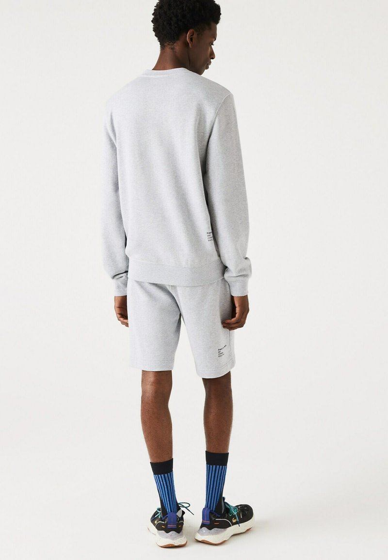 Sweat-shirt gris et shorts en tissu mélangé coton. Présente des poignets côtelés, un design simple, et des chaussettes rayées bleues avec des baskets noires.