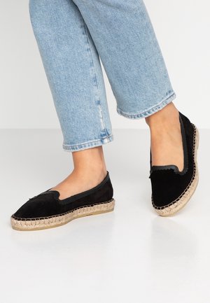 Espadrilles de ante negro con bordes ondulados y suela de yute natural, con un corte bajo y diseño flexible. Llevadas con jeans cropped de color azul claro.