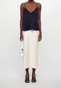 Camisole en satin bleu marine à décolleté en V, associé à une jupe midi en satin crème ; présente des bretelles fines et une finition lisse, complétée par des talons à lanières noirs.