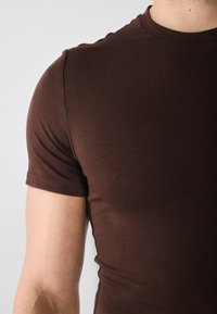 Barna, rövid ujjú póló, amely puha, könnyű anyagból készült; feszes fazon, sima textúrával és klasszikus kerek nyakkivágással.