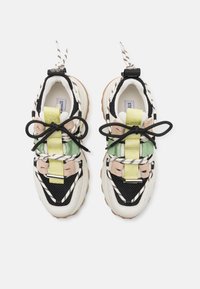Baskets épaisses avec des panneaux blancs, noirs, verts et beiges, des lacets rayés noirs et blancs, et des sangles jaune-vert griffées "STEVE MADDEN".