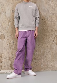 Grå Nike-tröja, lila baggybyxor, vita sneakers med rosa detaljer. Släta texturer, avslappnad passform, kontrasterande färger.