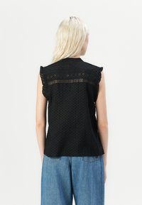 Top fără mâneci, de culoare neagră, cu un model texturat cu puncte, dantelă decorativă cu decupaj și o croială confortabilă. Spatele are un detaliu cusut de-a lungul gâtului.