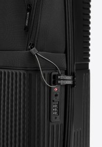 Valise noire avec une surface texturée, deux zippers, un mécanisme de verrouillage ajustable et une étiquette de marque bien visible.