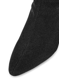 Černá strukturovaná bota s špičatou špičkou a elegantním designem. Materiál má jemný lesk a viditelné švy podél okrajů.