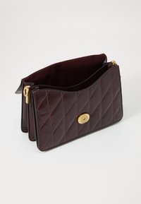 Quilted burgundy leather handbag with a textured surface, gold circular hardware, and a soft interior. Features a flap closure and dual compartments.