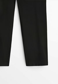 Pantalon noir à jambe droite, visible de la mi-cuisse à l'ourlet, sur un fond blanc.