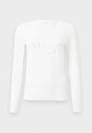 Hvit langermet t-skjorte med V-hals, med preget "Guess"-logo og "est. 1981" i metalliske detaljer. Mykt bomullsmateriale.