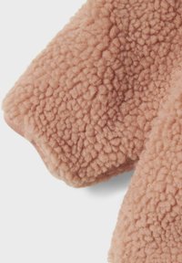 Mekanizam, teksturirana prašnjavo roza fleece tkanina s mekankom, kovrčavom površinom koja se proteže s ruba rukava od odjeće.