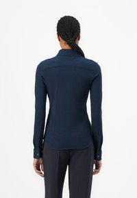 Camicetta blu navy a maniche lunghe con colletto, vestibilità slim, dettaglio sulla spalla posteriore e polsini con bottoni; tessuto liscio e leggero.