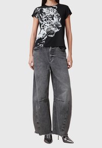 T-shirt noir avec un graphisme de léopard, associé à un jean gris large et déchiré, et des chaussures à talons hauts noires et brillantes.