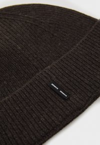 Brown knitted beanie hat with ribbed texture; features a small black label with white text on the side.
