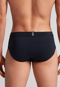 Námořnické plavky se hladkým povrchem a přiléhavým střihem, s minimalistickou značkovou nálepkou na zadní straně.