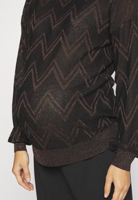 Maglione nero a texture con un motivo a zigzag in bronzo, con maniche lunghe e polsini a coste, progettato per adattarsi a una pancia in crescita.