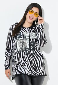 Langarm-Hoodie mit schwarz-weißem Zebra-Streifenmuster, ausgestattet mit grafischen Drucken und einer Kordelzugkapuze. Weiches Material, lässige Passform.