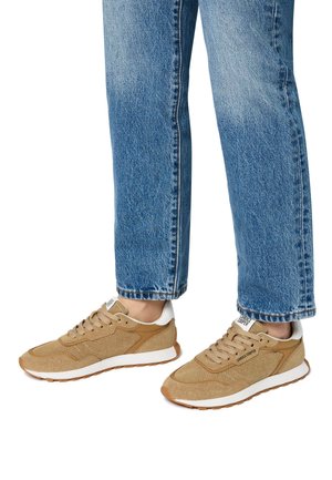 Sneaker beige in materiali mesh e suede, con dettagli bianchi e suole in gomma. Indossate con jeans blu risvoltati, che mostrano uno stile casual.
