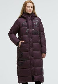 Long purple puffer coat with quilted design, black printed text accents, hood, and zippered pockets. Smooth, shiny texture.