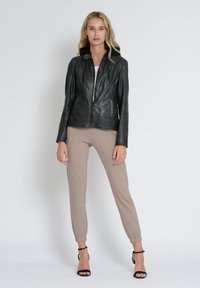 Schwarze Lederjacke mit tailliertem Design, Reißverschlussfront und detaillierten Nähten, kombiniert mit beigen Jogginghosen und schwarzen geschnürten Absätzen.