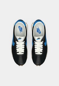 Sapatilhas Nike pretas e azuis com atacadores brancos, apresentando uma textura suave, logo distinto e uma silhueta clássica. A sola apresenta detalhes de tração.