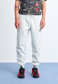 Grå sweatshirtbukser med elastisk talje, prydet med et sort Jumpman-logo nederst til venstre. Matcher med sorte og røde sneakers.