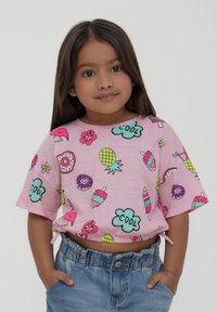 Maglietta corta rosa con stampe colorate di ciambelle, gelato, fiori e testi giocosi. Abbinata a pantaloni corti di denim, che mostrano un fit rilassato.