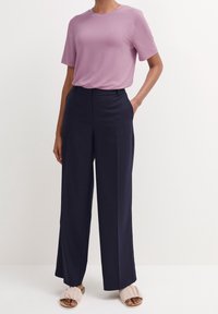 T-shirt lilas clair à manches courtes associé à un pantalon large bleu marine et des sandales à semelle beige douces, présentant une coupe décontractée et un design minimaliste.