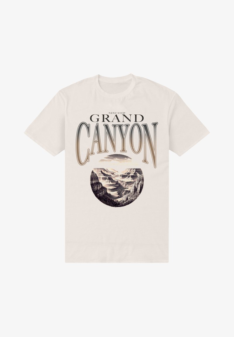 Cremefarvet t-shirt med et rundt grafisk billede af Grand Canyon, med sort tekst ovenfor og nedenfor, der forestiller bjerglandskaber.