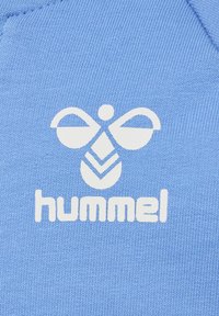 Ljust blå sweatshirtmaterial med en vit Hummel-logotyp som har en stiliserad bi-design och fetstilta bokstäver, vilket visar en jämn textur.