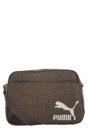 Bruine, getextureerde Puma schoudertas met wit Puma-logo en verstelbare donkerbruine band tegen een witte achtergrond.