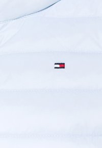 Tissu matelassé bleu clair avec de petites coutures horizontales et un logo rectangulaire centré en fil blanc, rouge et noir.