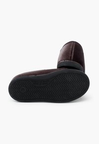 Pantofole in velluto marrone con forma curvata e suola in gomma. Include una suola esterna nera testurizzata e dettagli cuciti lungo i bordi.