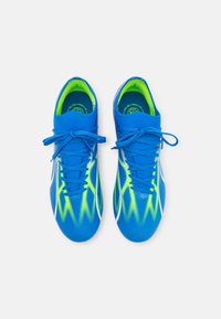 Zapatillas deportivas azules con acentos amarillos, que cuentan con una parte superior de malla texturizada, cordones simétricos y un diseño aerodinámico.