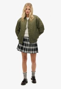 Oliwkowa bomberka, biała sweter, mini spódniczka w kratę w kolorach czarnym, białym i szarym, szare skarpetki w czarno-białe paski, czarne buty.