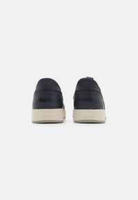 Navy blue leather sneakers with a beige rubber sole, rounded shape, and minimal accents. Features a pull tab on the heel for ease of wear.