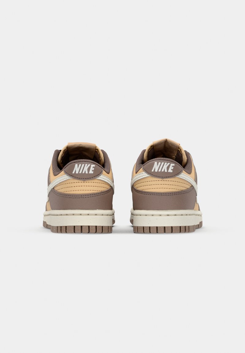 Baskets Nike avec une palette de couleurs beige et marron, présentant une tige en cuir texturé, un collier rembourré et une semelle en caoutchouc avec un motif de bande de roulement visible.