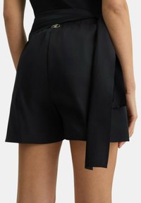 Pantaloni neri realizzati in un tessuto liscio. Presentano una cintura larga da annodare in vita e un orlo rifinito con cura. Design semplice e sartoriale.