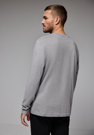 Chemise grise à manches longues en tissu doux, avec un col rond et une coupe décontractée, présentant des coutures visibles et une texture lisse.
