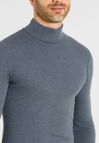 Maglione grigio a collo alto in tessuto a coste. Presenta un design aderente con maniche lunghe e un collo alto. Texture morbida.