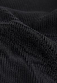 Čierna rebrovaná tkanina s textúrovaným povrchom a konzistentnými vertikálnymi líniami, vystihujúca mäkký, elastický materiál.